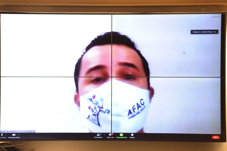 Homem usa máscara branca e olha para a câmera do computador