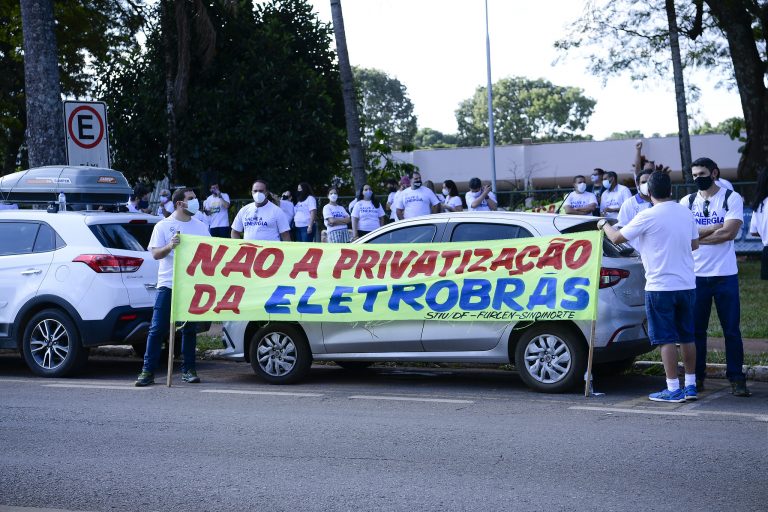 Trabalhadores protestam contra privatização da Eletrobras. Eles seguram uma faixa e estão em pé num gramado