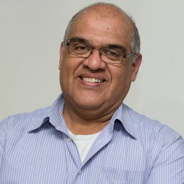 Marengo é um homem branco, calvo e grisalho; ele usa óculos quadrados e veste uma camisa listrada azul e branca; ele está sorrindo