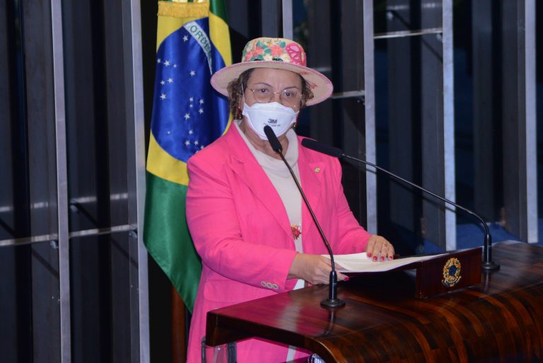 Deputada Tereza Nelma fala ao microfone. Ela usa máscara branca e blazer e chapéu rosa