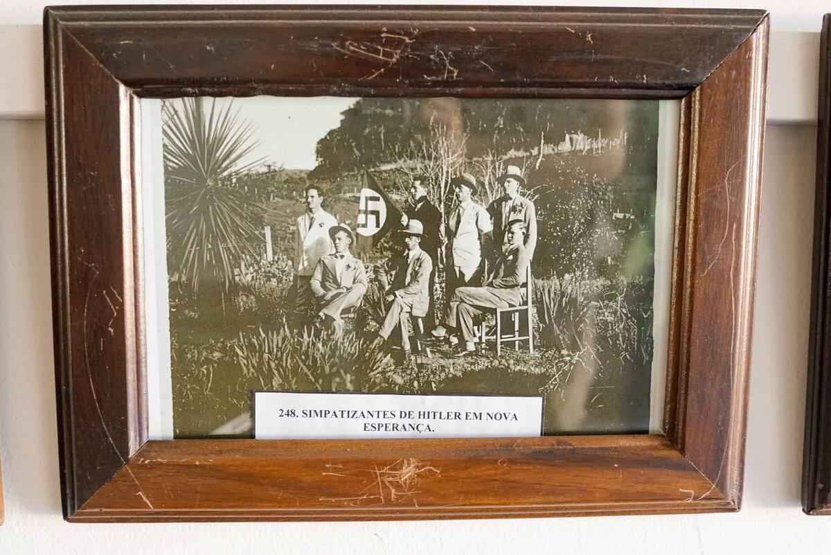 Imagem exposta no corredor mostra homens ''simpatizantes de Hitler'' (como dito no papel posto em frente a foto), eles posam junto a uma bandeira com uma suástica.