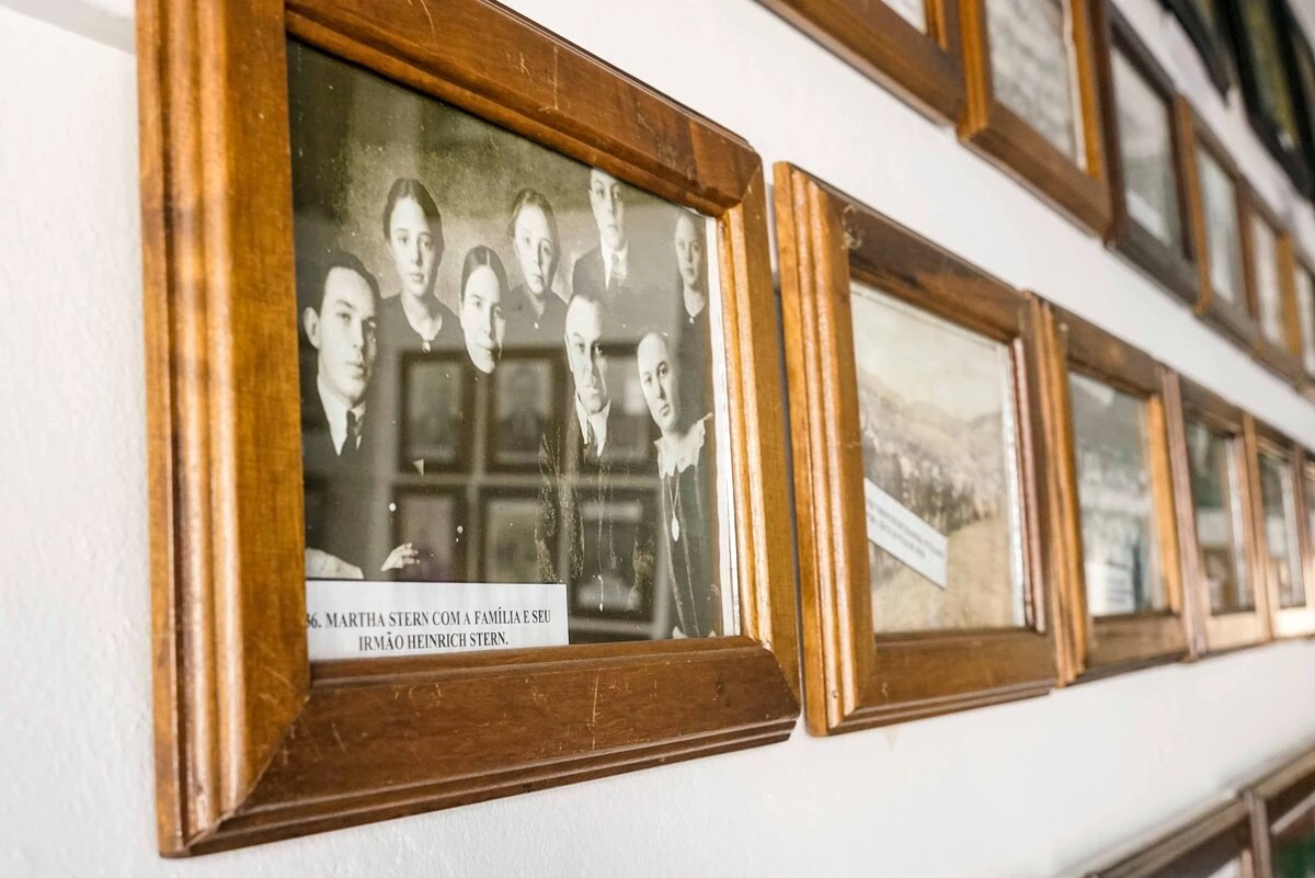 A imagem mostra o corredor com as fotos expostas, e em primeiro plano a foto de uma família.