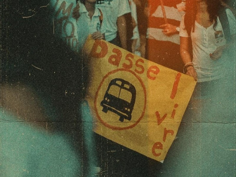 Manifestação contra o aumento da passagem dos transportes, na imagem duas pessoas seguram um cartaz com um ônibus desenhado escrito ''Passe Livre!''